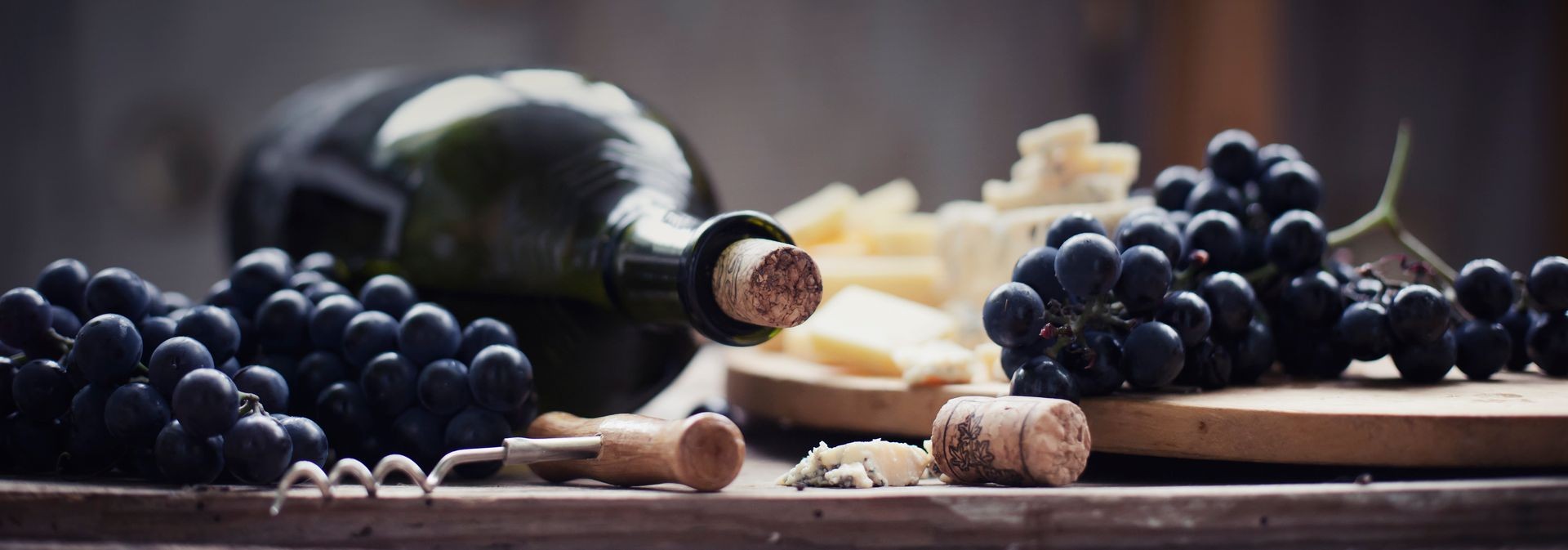 red wine background with corkscrew, grapes and cheese on wooden background
